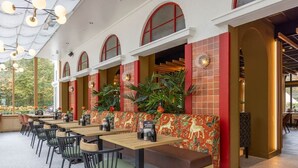 Un espace de restauration en plein air avec de longues tables en bois, des chaises noires et des murs en briques rouges.