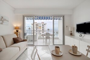 Moderni hotellihuone, jossa on parveke, sohva, ruokapöytä kupeineen ja televisio.