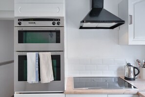 A kitchen with two ovens, a black range hood, a stainless steel kettle, and a wooden countertop.