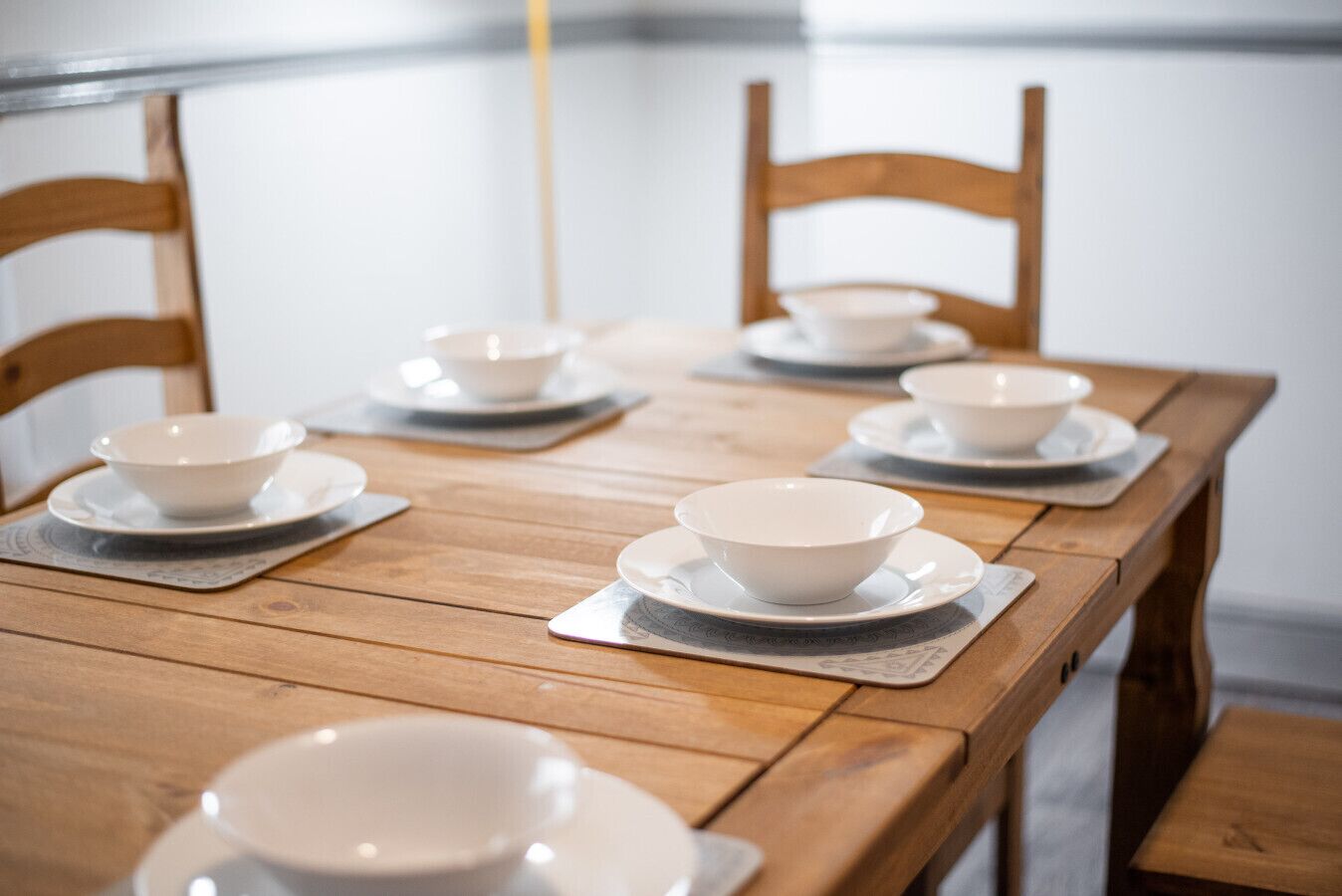 A wooden dining table with white bowls and saucers.