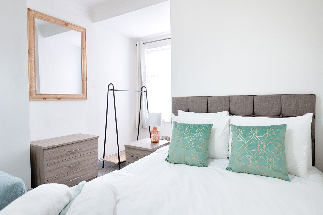 A bedroom with a bed, a dresser, a mirror, a window, and a nightstand.