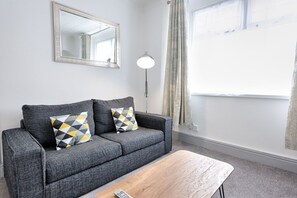 A grey sofa with patterned cushions, a wooden coffee table, a floor lamp, and a mirror on the wall.