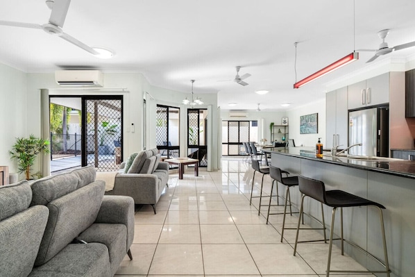 A modern kitchen with a bar area, a dining table, and a seating area with sofas. - Zen Orient Luxurious 4BR Oasis With Private Pool (Darwin)