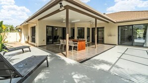 A covered patio area with a table and chairs, a bench, and a poolside area.