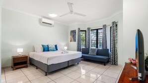 A bedroom with a bed, a sofa, a desk, a ceiling fan, and a window with curtains.