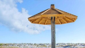 A wooden beach umbrella structure with a simple design, standing on a sandy surface with a clear sky in the background. - New Luxury Gulf Front Home | Event Friendly | Elevator | Sleeps 24 (Pensacola Beach)