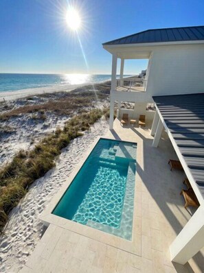 Ein Pool mit klarem Wasser, Blick auf einen Strand und eine überdachte Sitzgelegenheit im Freien.
