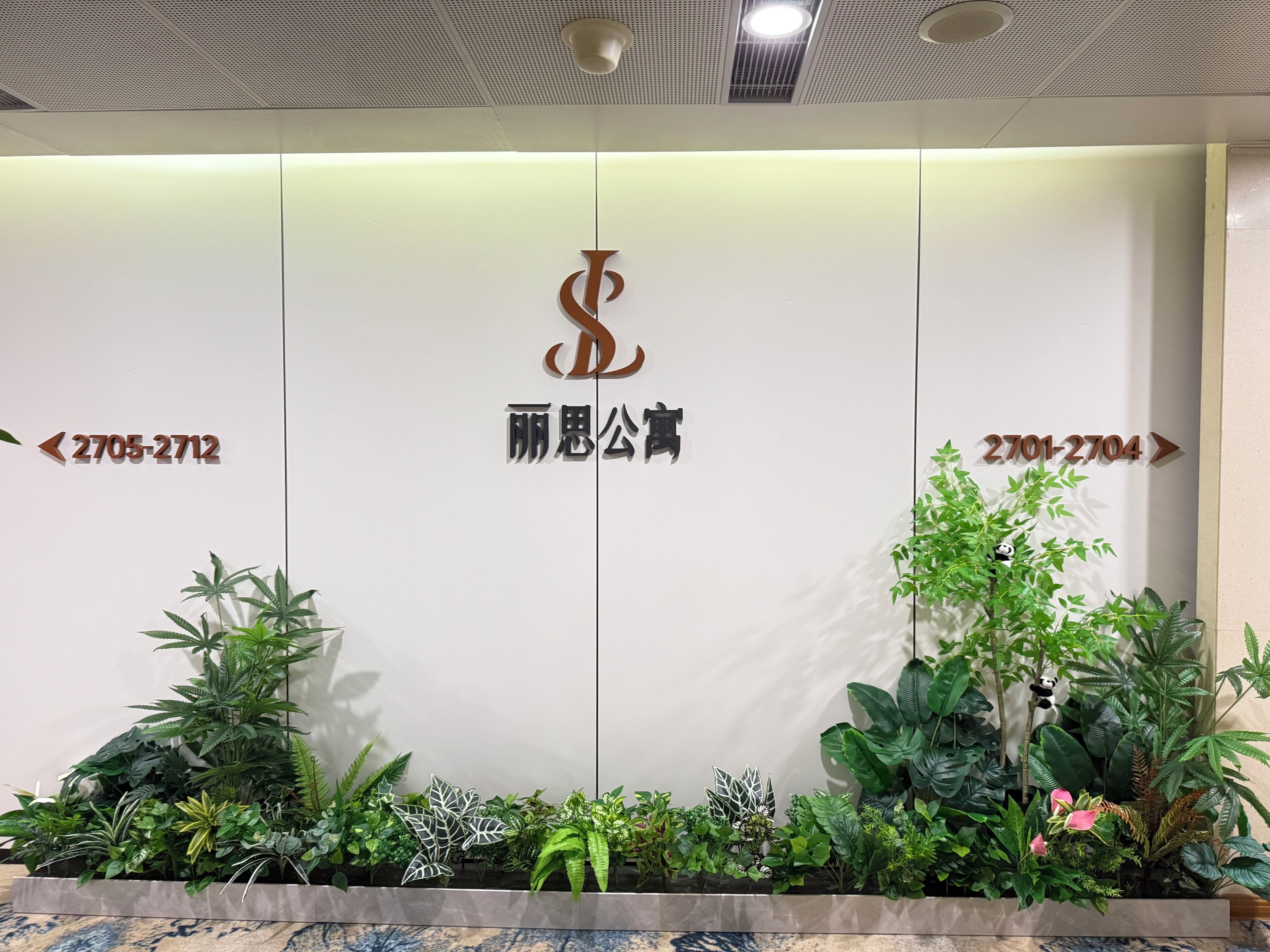 A reception desk with a logo, directional arrows, and a plant arrangement.