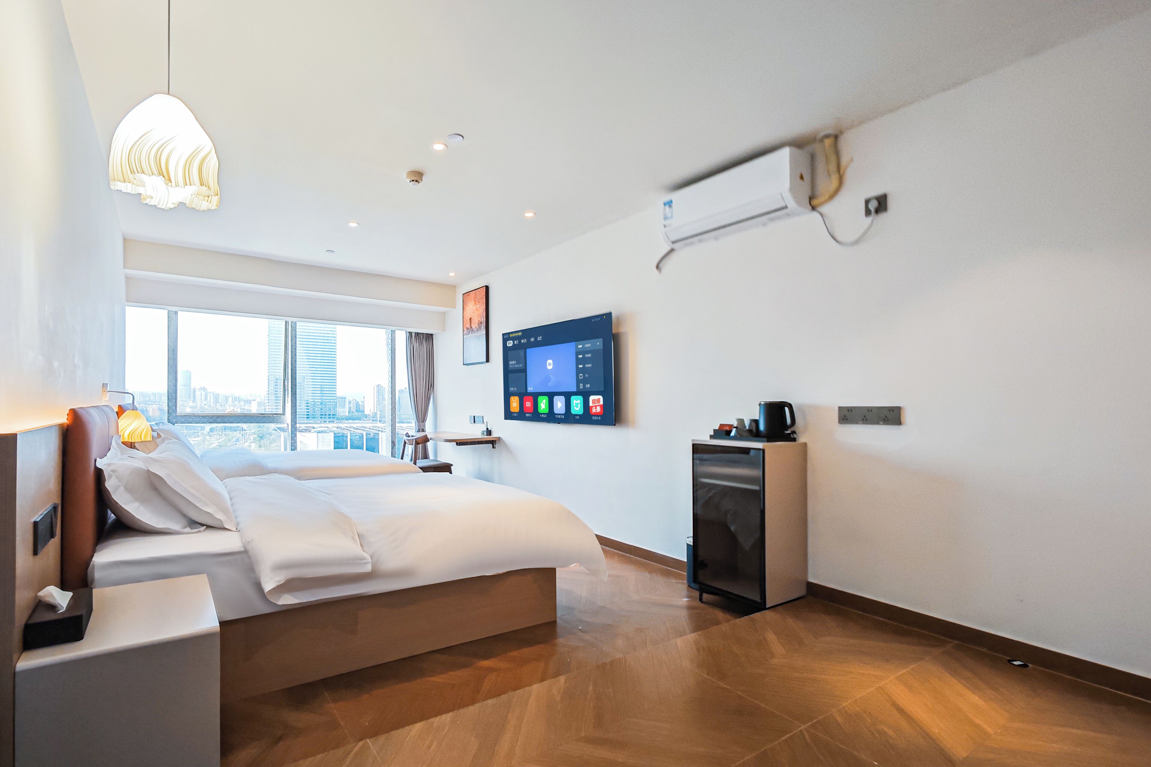 A modern hotel room with a large bed, a flat-screen TV, a minibar, and a city view.
