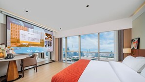 A hotel room with a bed, a desk, a chair, a TV, and a large window with a city view. - Ritz Star City View Residence  (Guangzhou)
