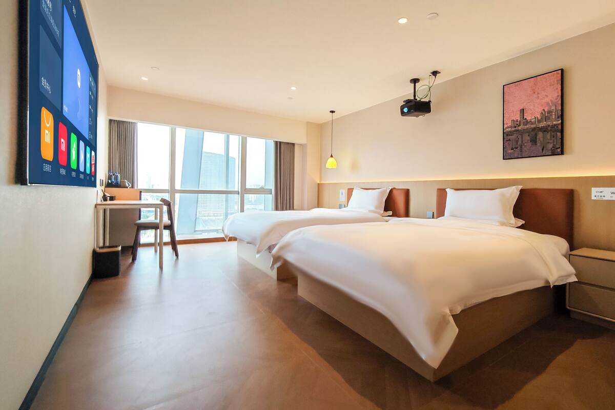 A hotel room with two beds, a desk, a chair, and a large window.