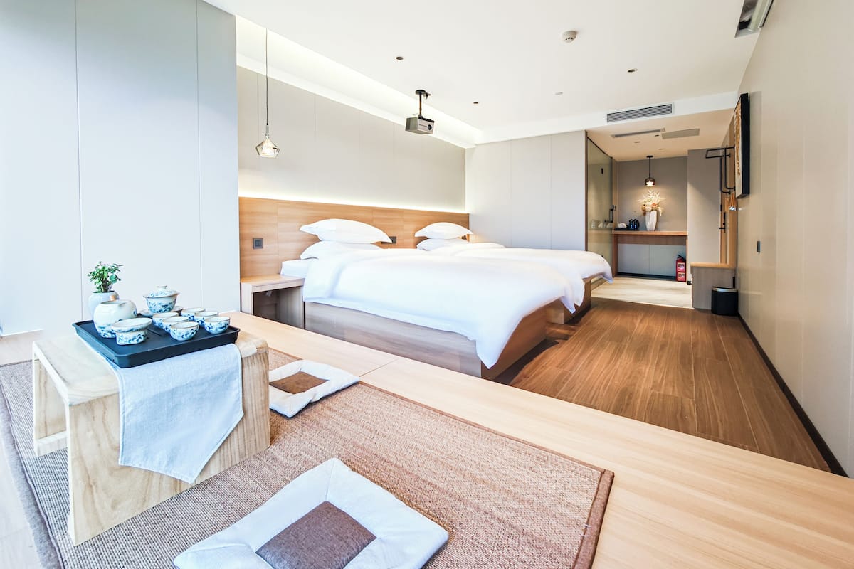 A modern hotel room with a large bed, a small desk with a tray of bowls, a mirror, and a TV mounted on the wall.