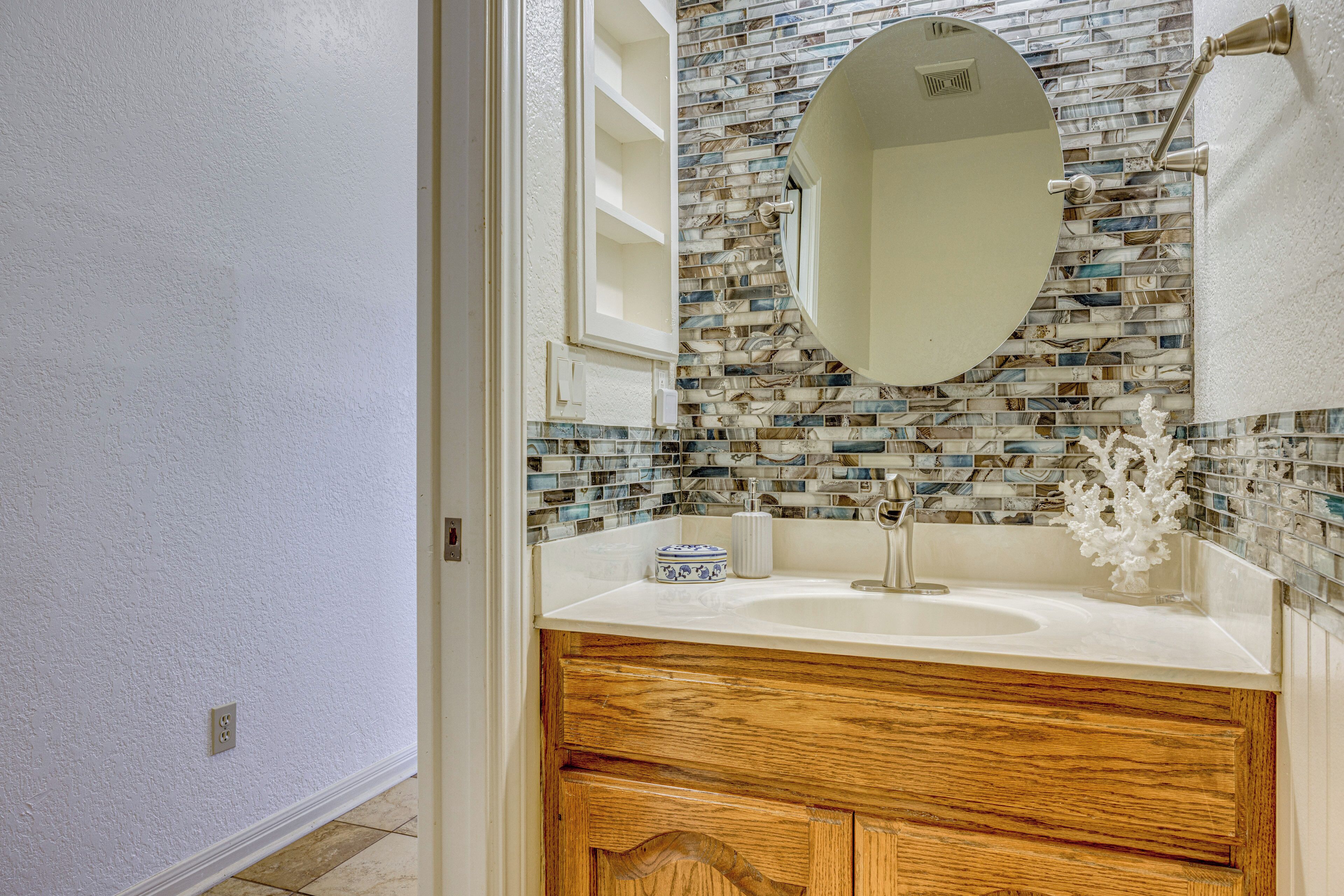 A bathroom with a white sink, wooden vanity, a mirror, and a mosaic tile backsplash.