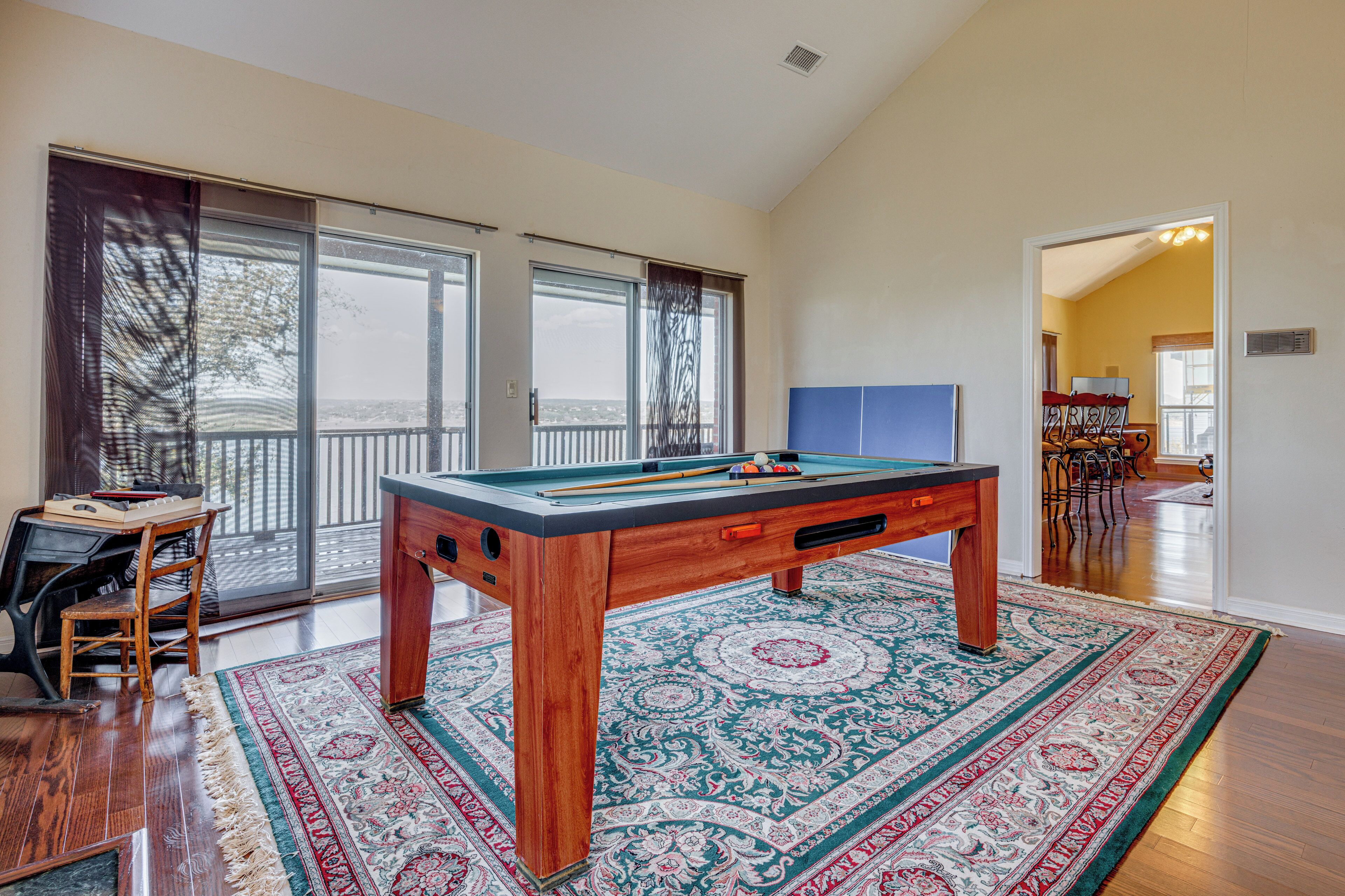 A pool table in a spacious room with a large window, a dining area, and a view of the outdoors.