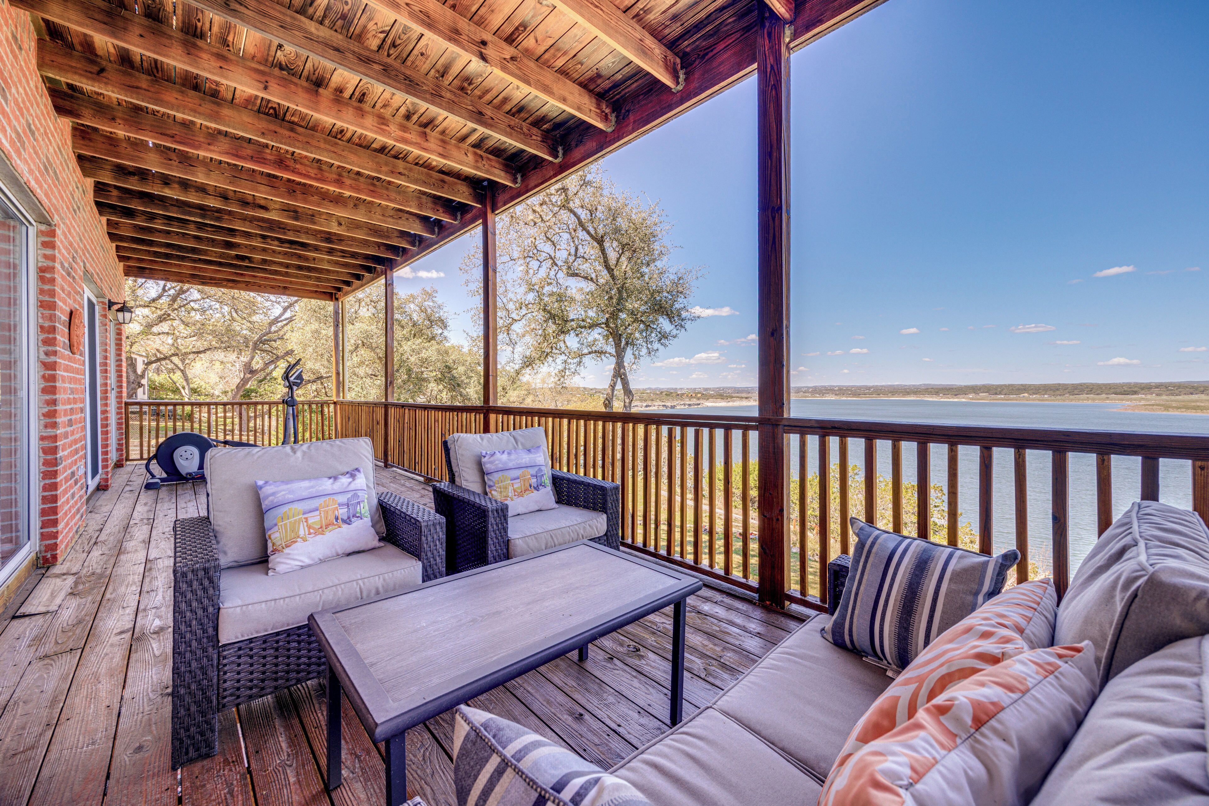 A covered outdoor deck with wicker furniture, a table, and a view of a body of water.