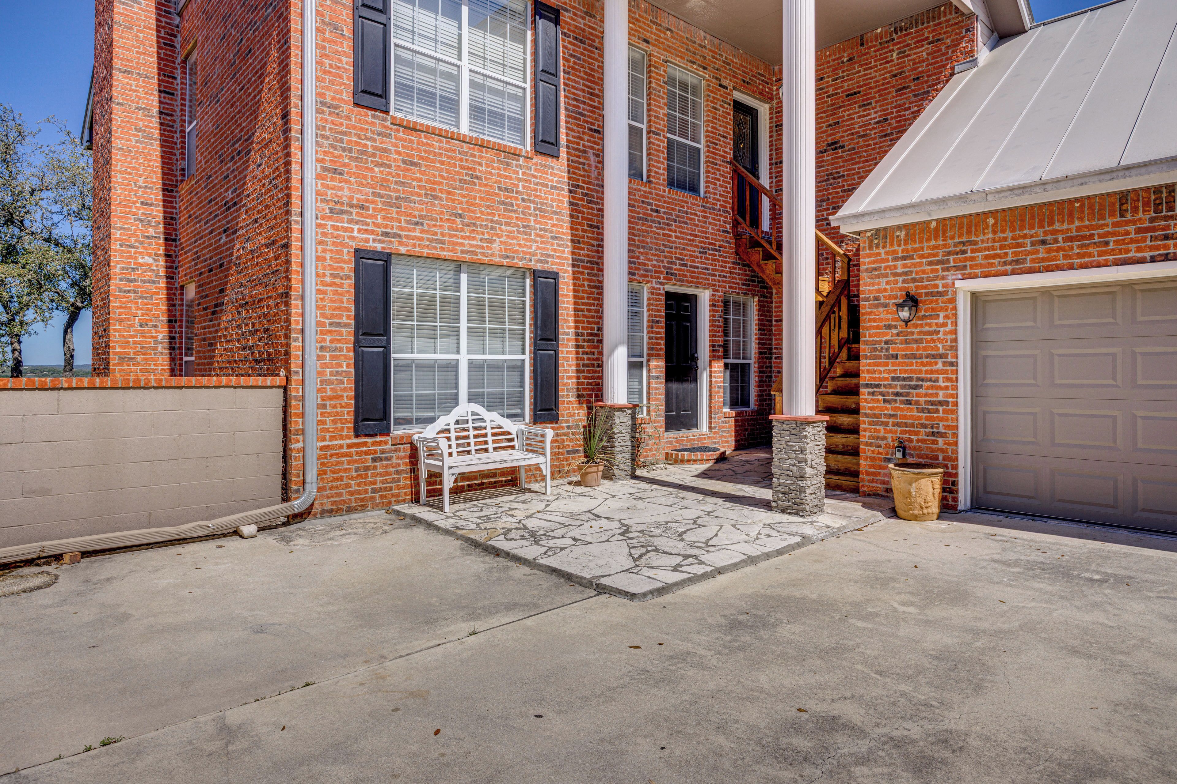 A two-story brick building with a garage, a white bench, and a stone-paved patio.