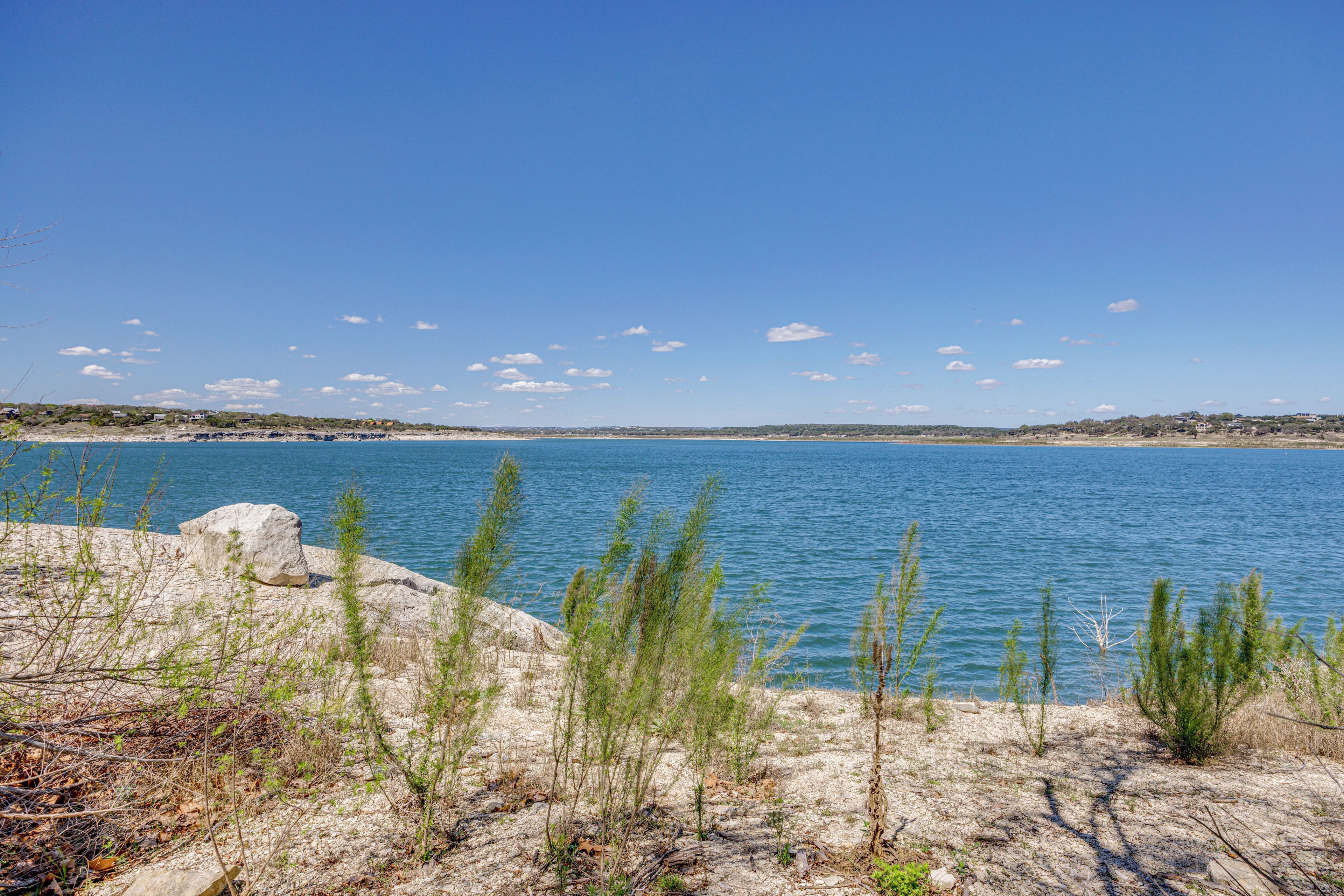 A coastal landscape with a clear sky, calm water, and sparse vegetation.