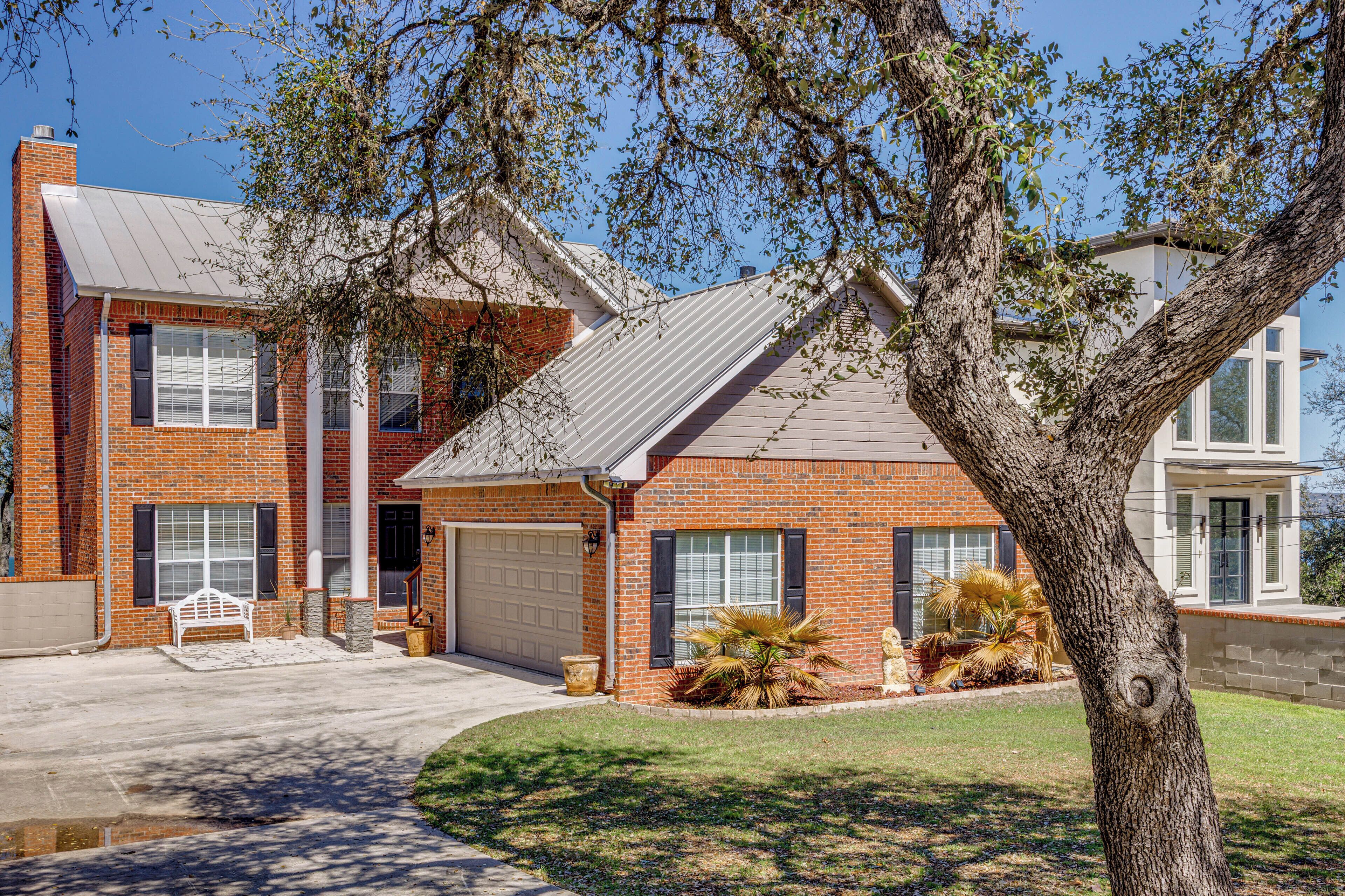 A two-story house with a garage, a tree in the front yard, and a bench.