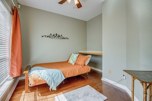 Un dormitorio con cama, una mesa de madera, un adorno de pared y una ventana con persianas.