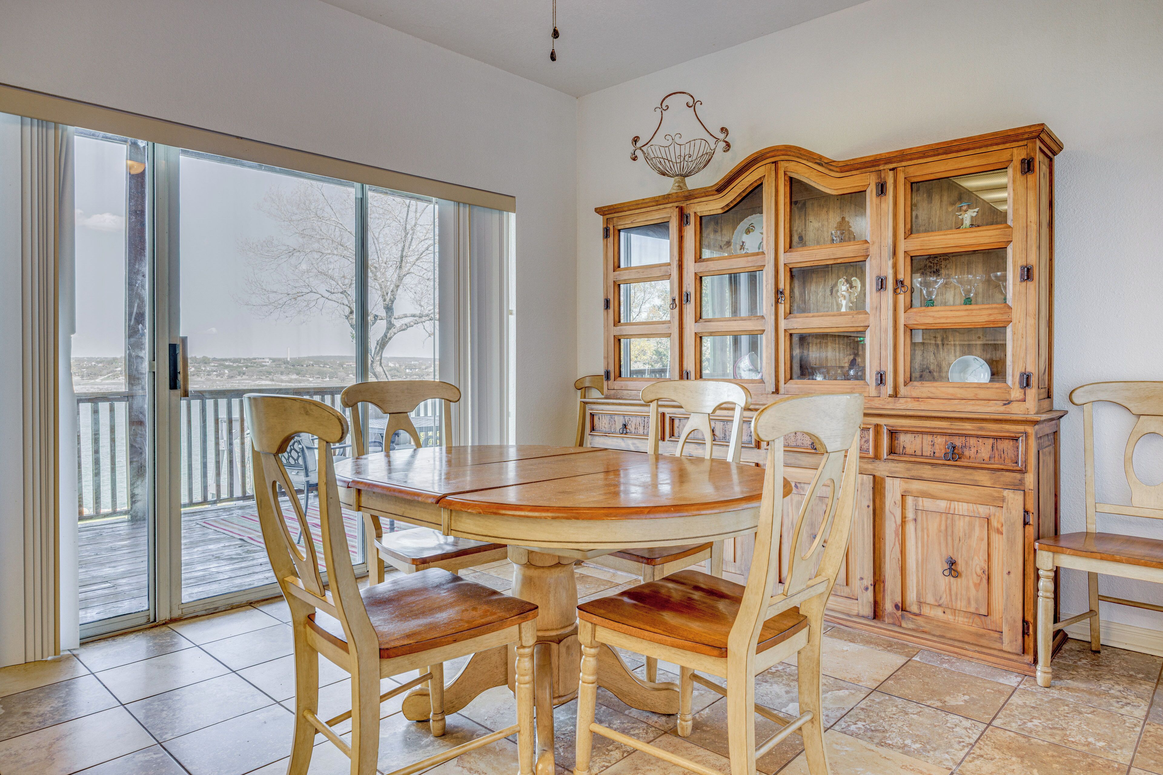 A dining area with a wooden table and chairs, a glass cabinet with dishes, and a view through the glass door.