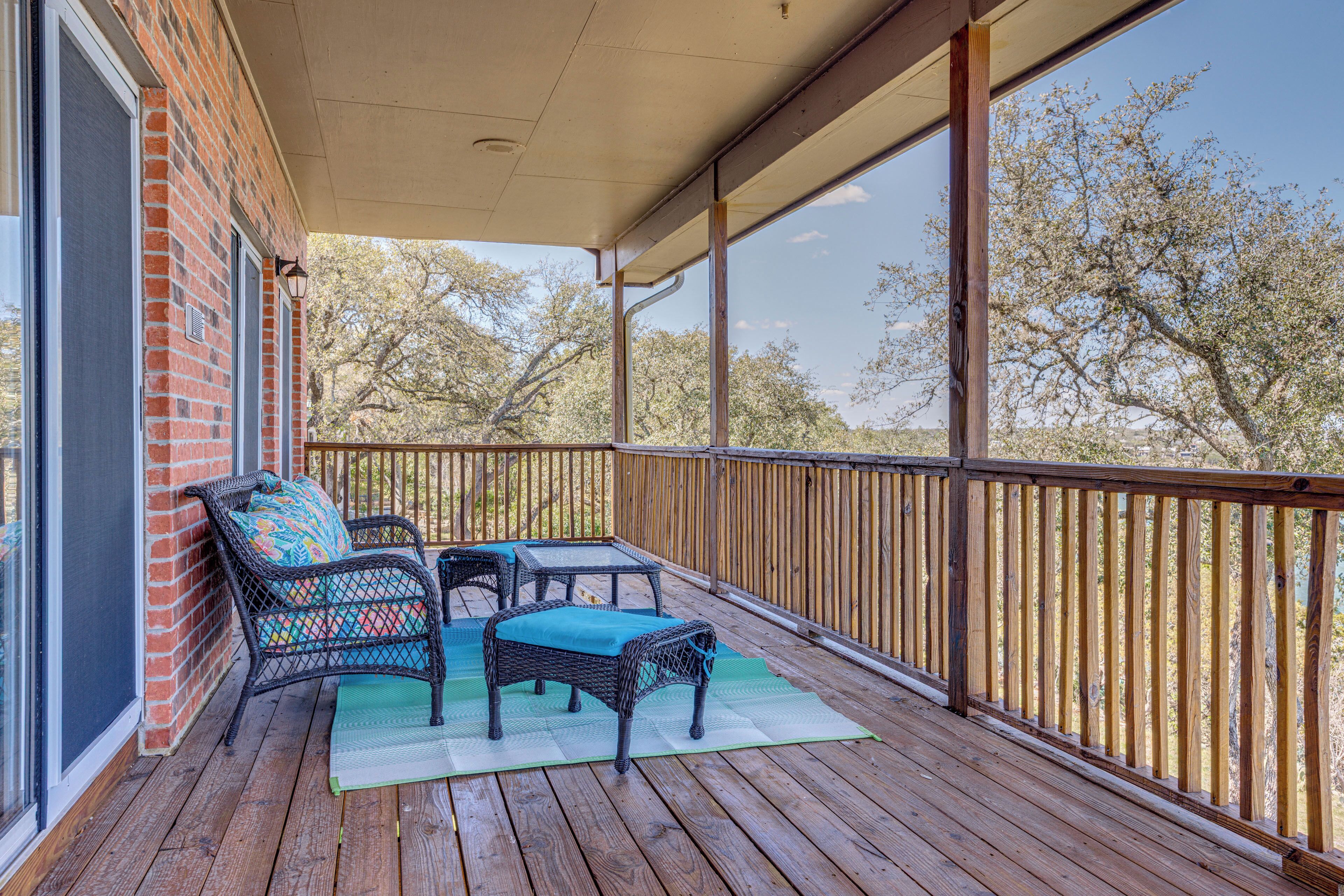 A covered outdoor area with a wooden deck, wicker furniture, and a view of trees.