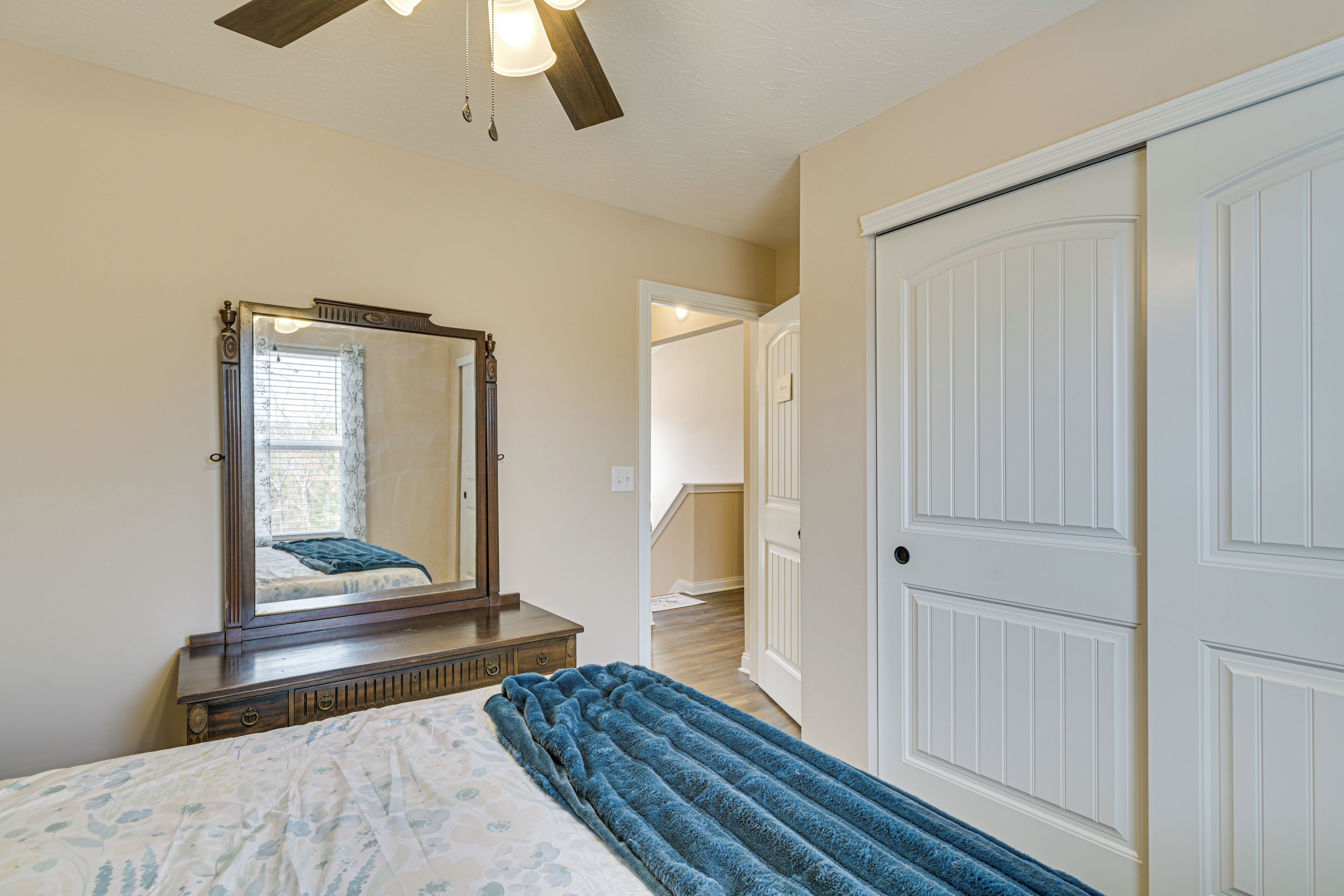 A bedroom with a bed, a dresser, a mirror, a door, and a staircase leading to another room.