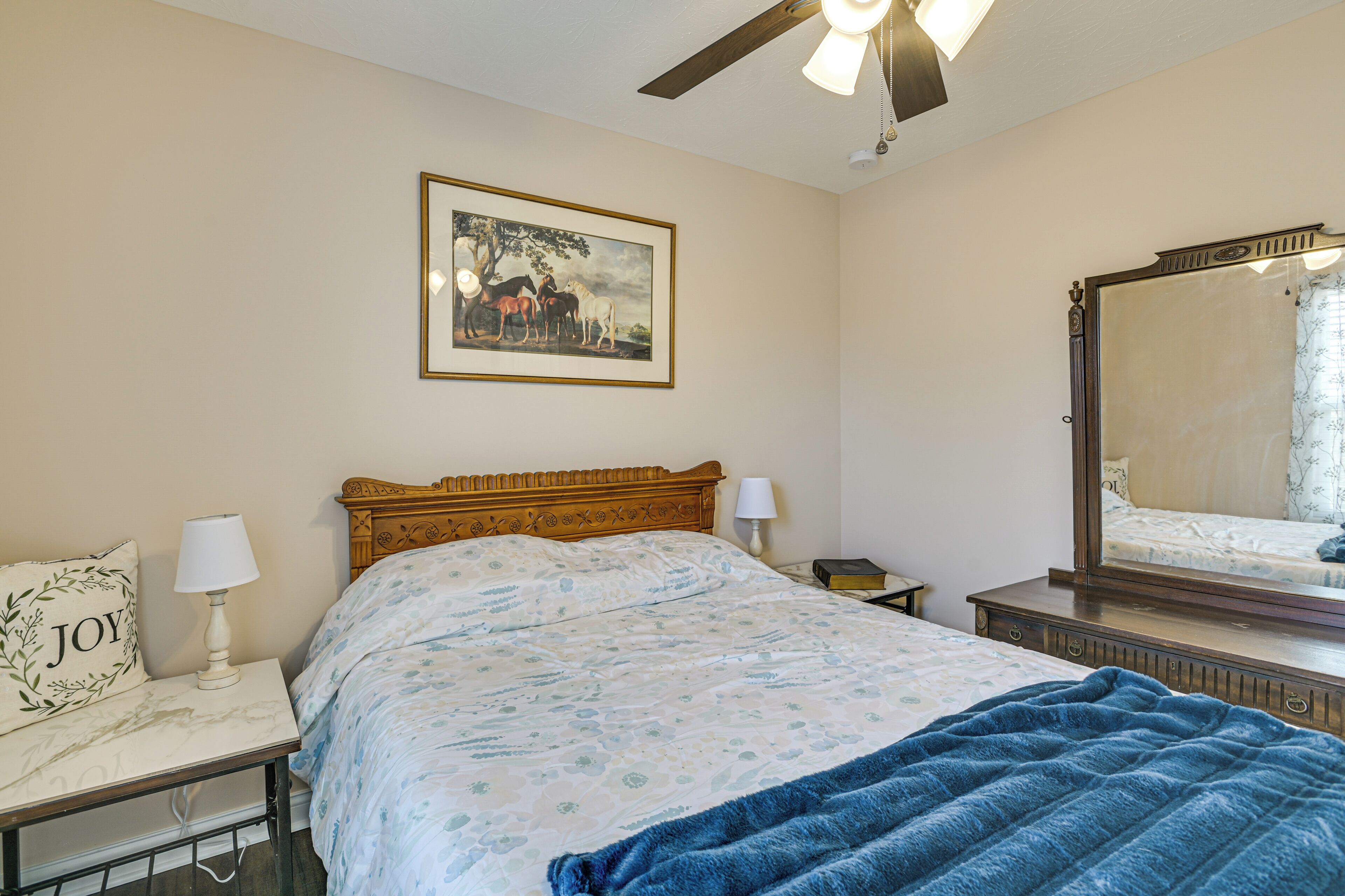 A bedroom with a bed, a nightstand, a lamp, a framed picture on the wall, and a ceiling fan.