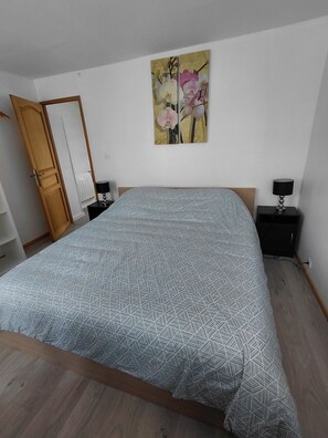 A bedroom with a bed, two bedside tables, a nightstand, a wooden wardrobe, and a painting on the wall. - A townhouse in a small town. (WATTEN)