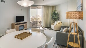 A modern living room with a round dining table, a sofa, a television, and a large window with a city view. - Walk to Beach - Palms of Destin Resort Unit (Destin)