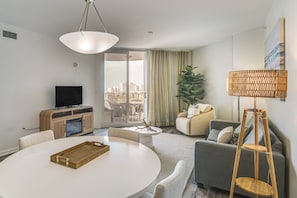A modern living room with a round dining table, a sofa, a television, and a large window with a city view. - Walk to Beach - Palms of Destin Resort Unit (Destin)