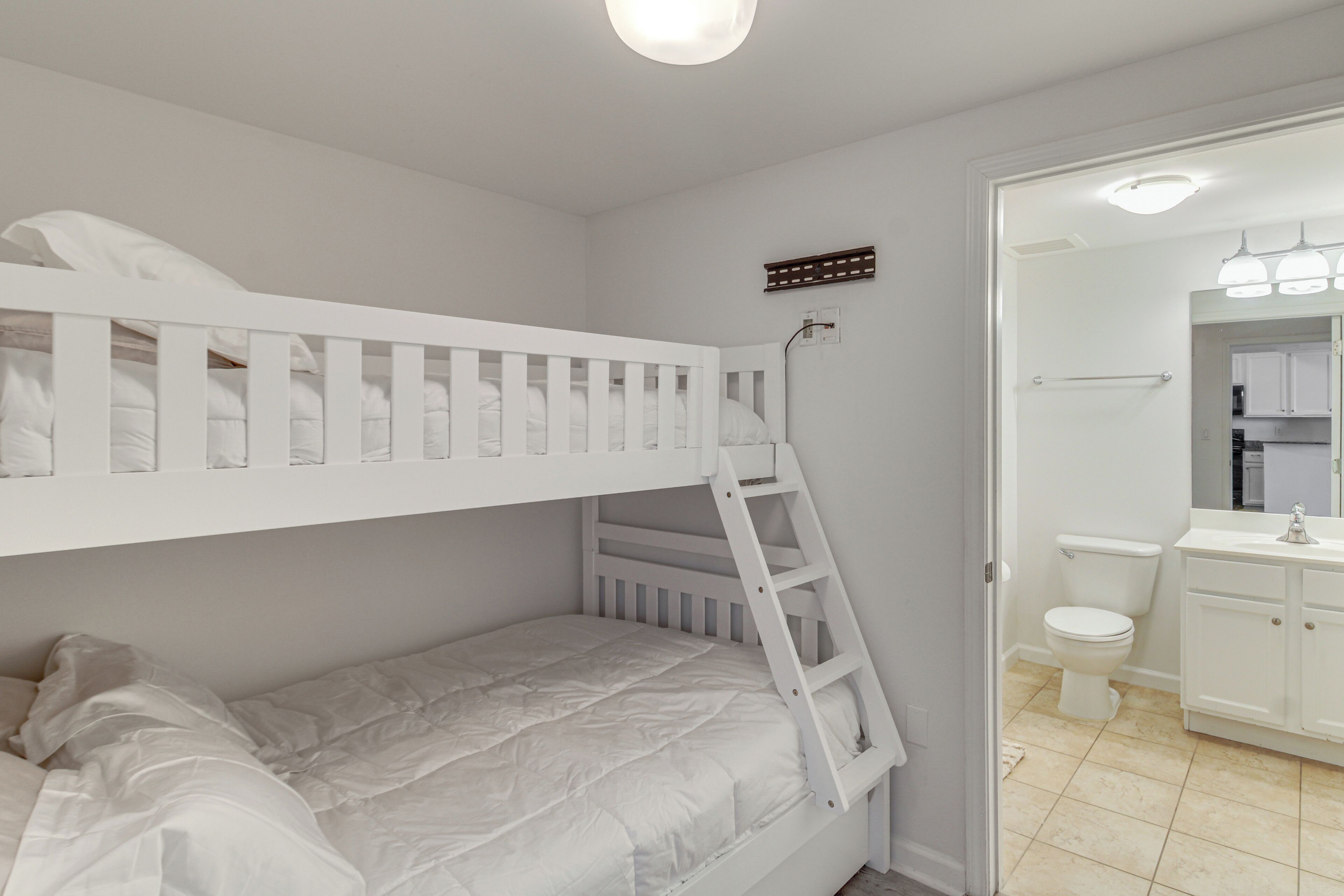Un lit superposé avec une échelle, des toilettes blanches et une salle de bain avec un lavabo et un miroir.
