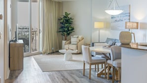 A modern living room with a sofa, dining table, chairs, a large potted plant, and a view through a sliding glass door. - Walk to Beach - Palms of Destin Resort Unit (Destin)