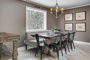 A dining area with a bench, table, chairs, a chandelier, framed pictures, and a window with a view of trees. - Sauna & Game Room! Tranquil Retreat on Grace Lake (Watersmeet)