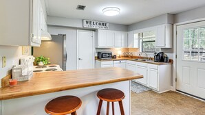 A kitchen with white cabinets, a wooden bar counter, two stools, a microwave, and a 'WELCOME FAMILY & FRIENDS' sign. - Families w/ Pets! Emerald Coast Home 9 Mi to Beach (Fort Walton Beach)