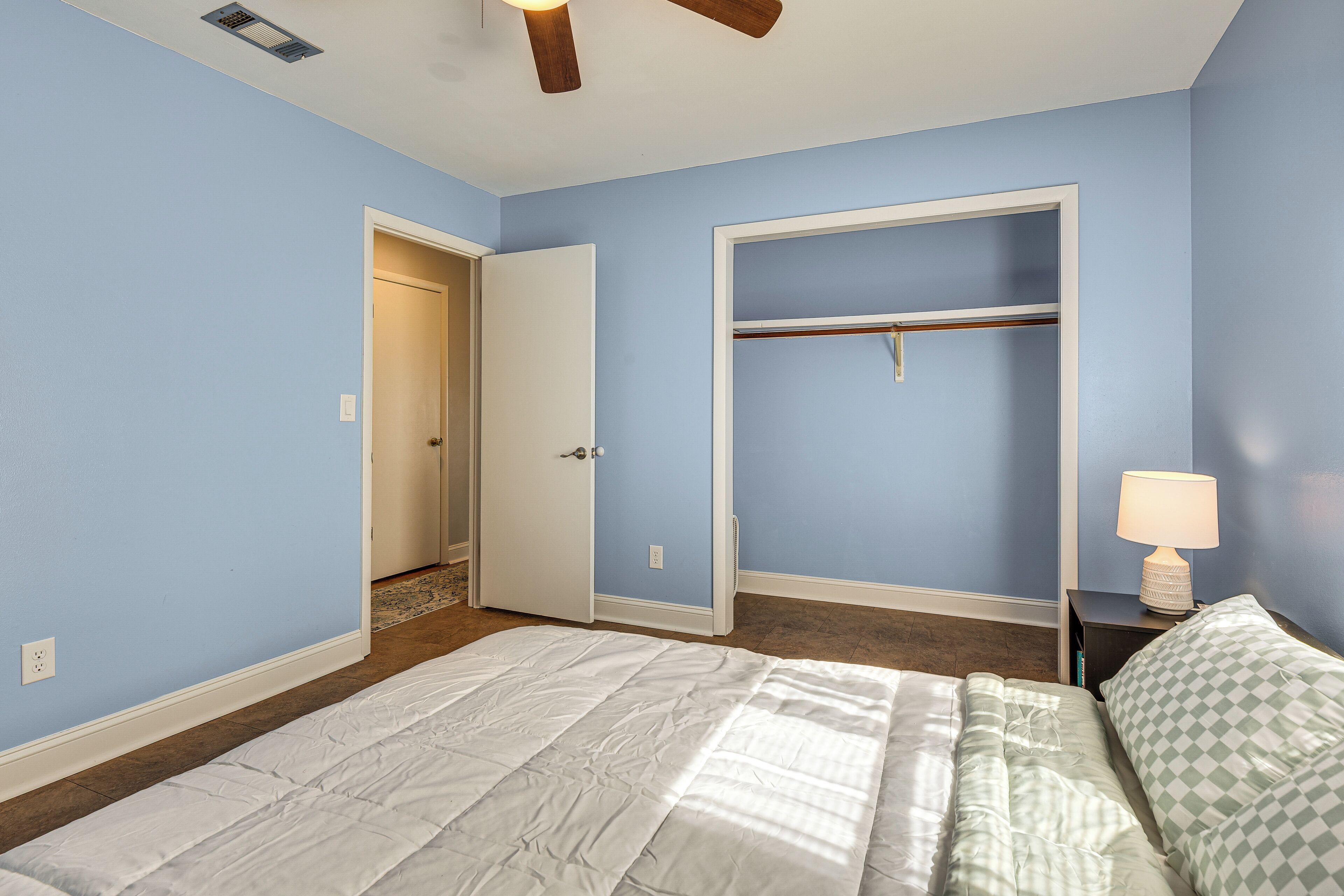 A bedroom with a bed, a closet, a nightstand with a lamp, and a ceiling fan.