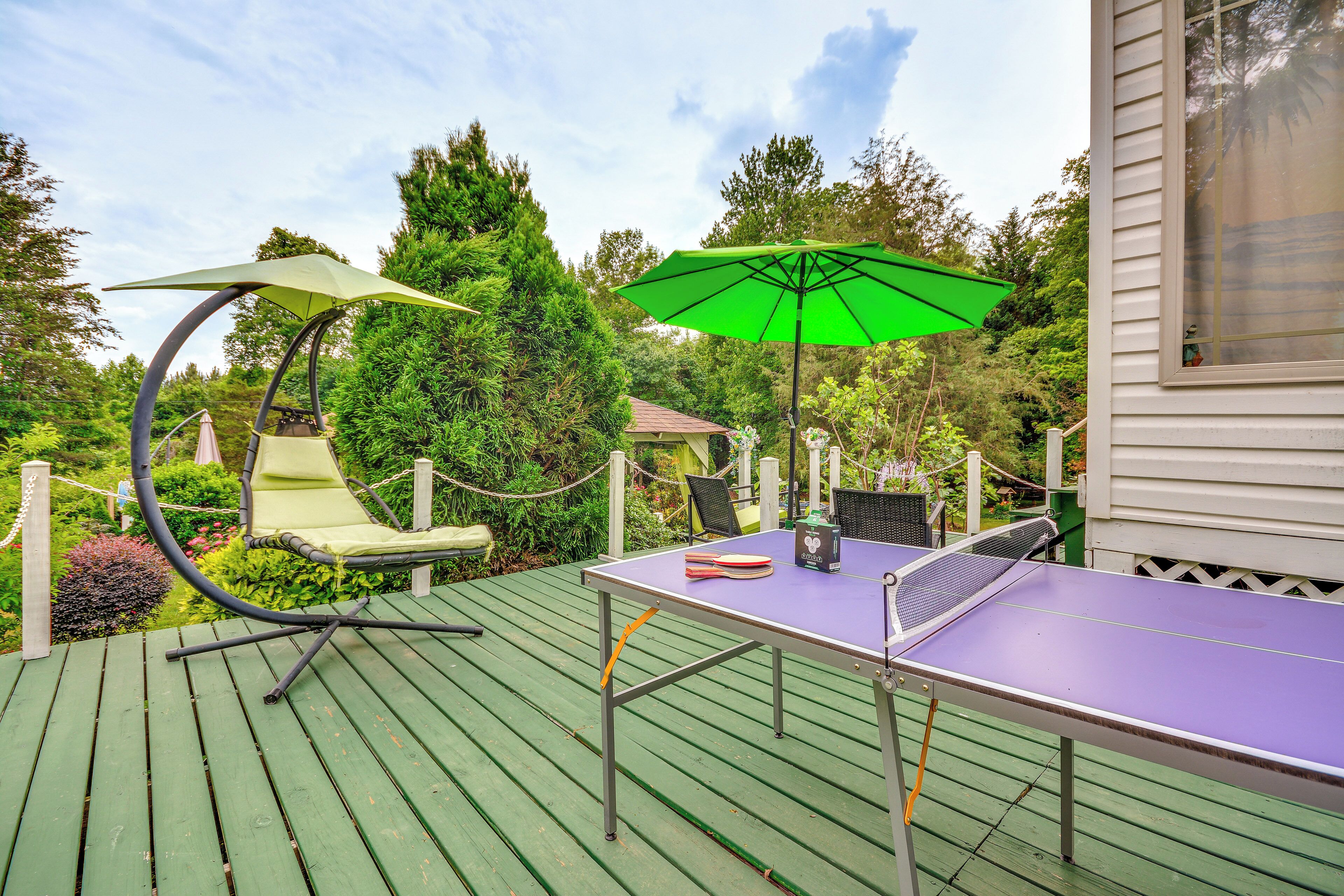 A ping pong table on a wooden deck with two chairs and a green umbrella.