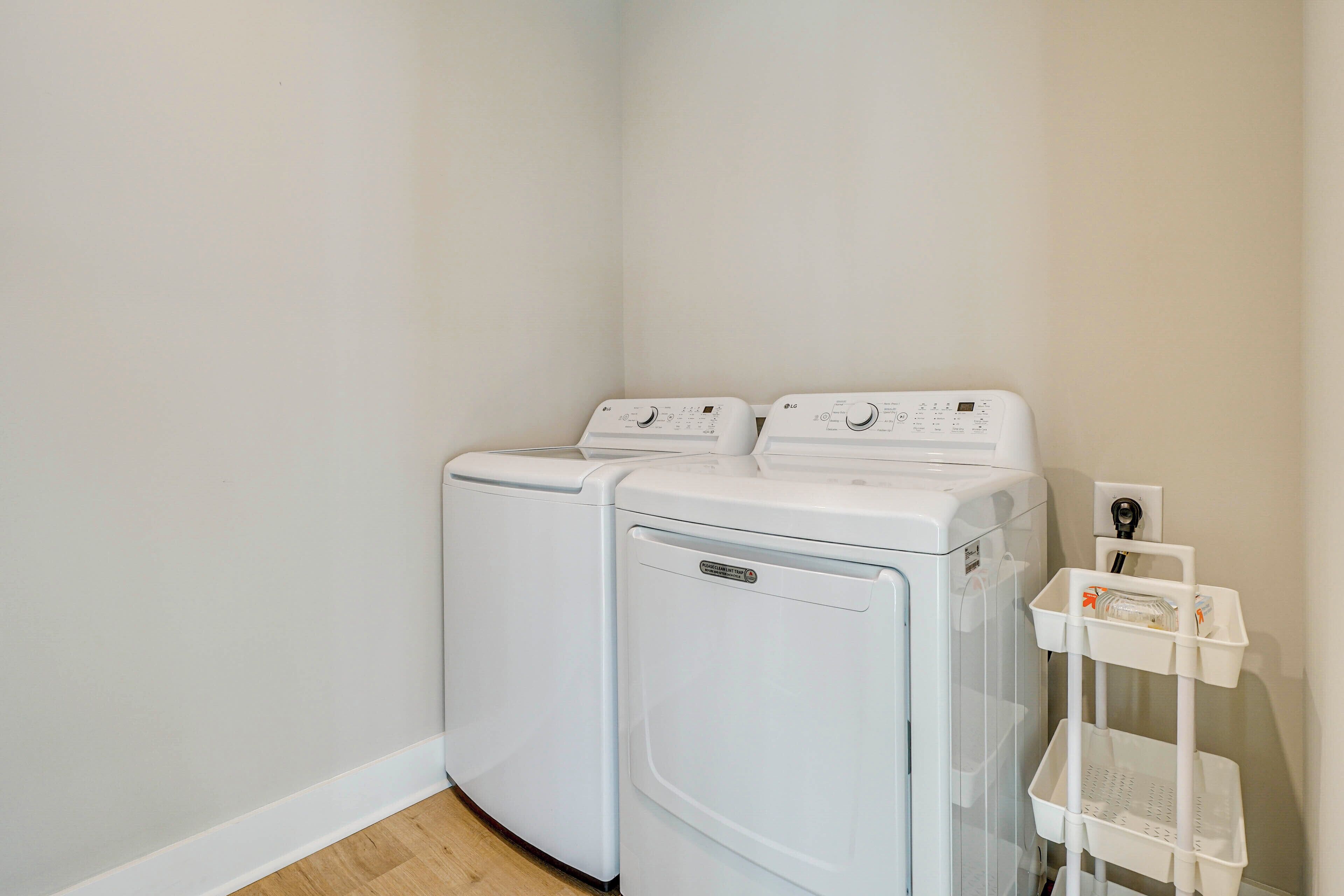 A laundry room with two stacked washers and dryers, a white wall, and a white shelf with a basket.