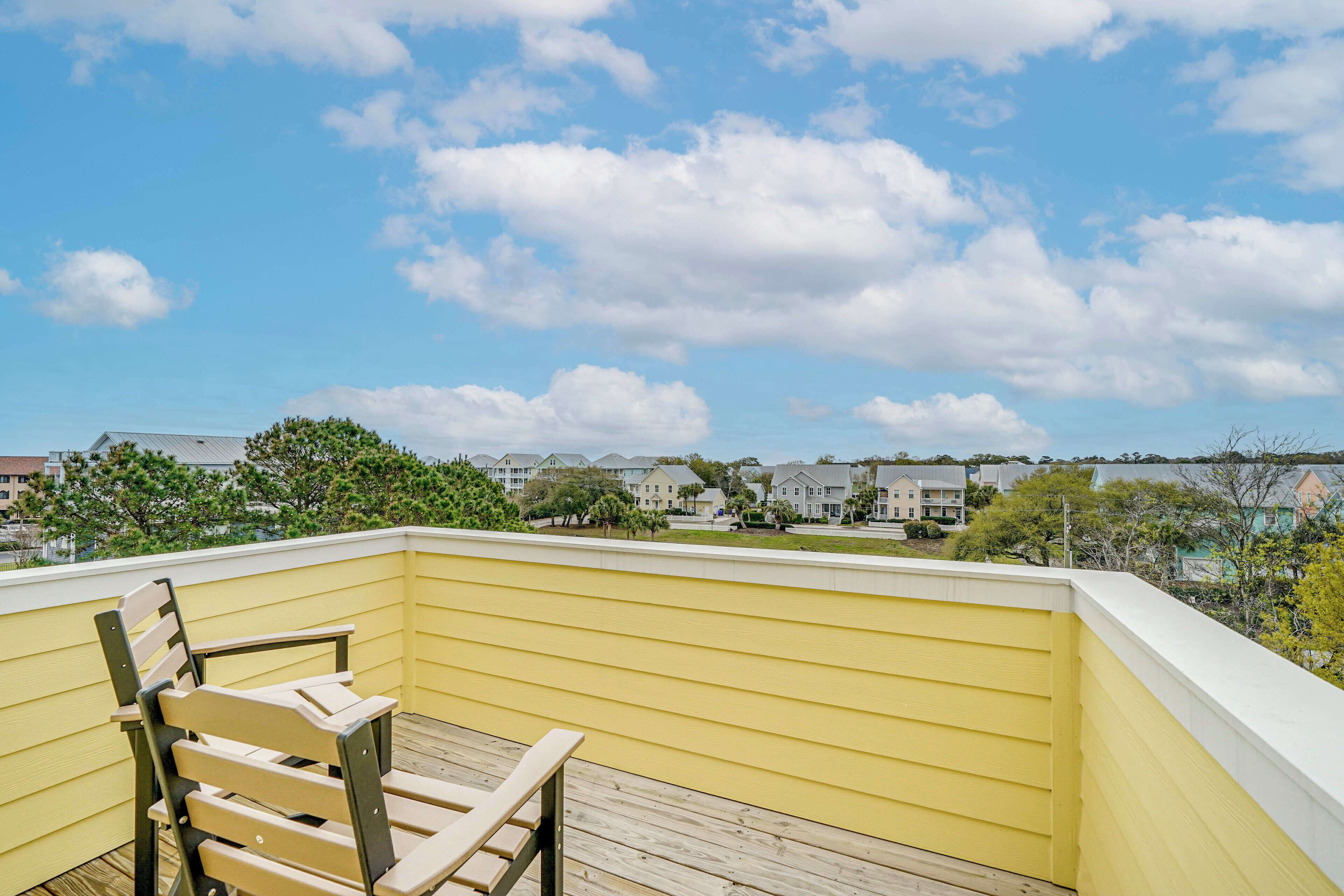 A balcony with a wooden chair, yellow siding, and a view of houses and trees.