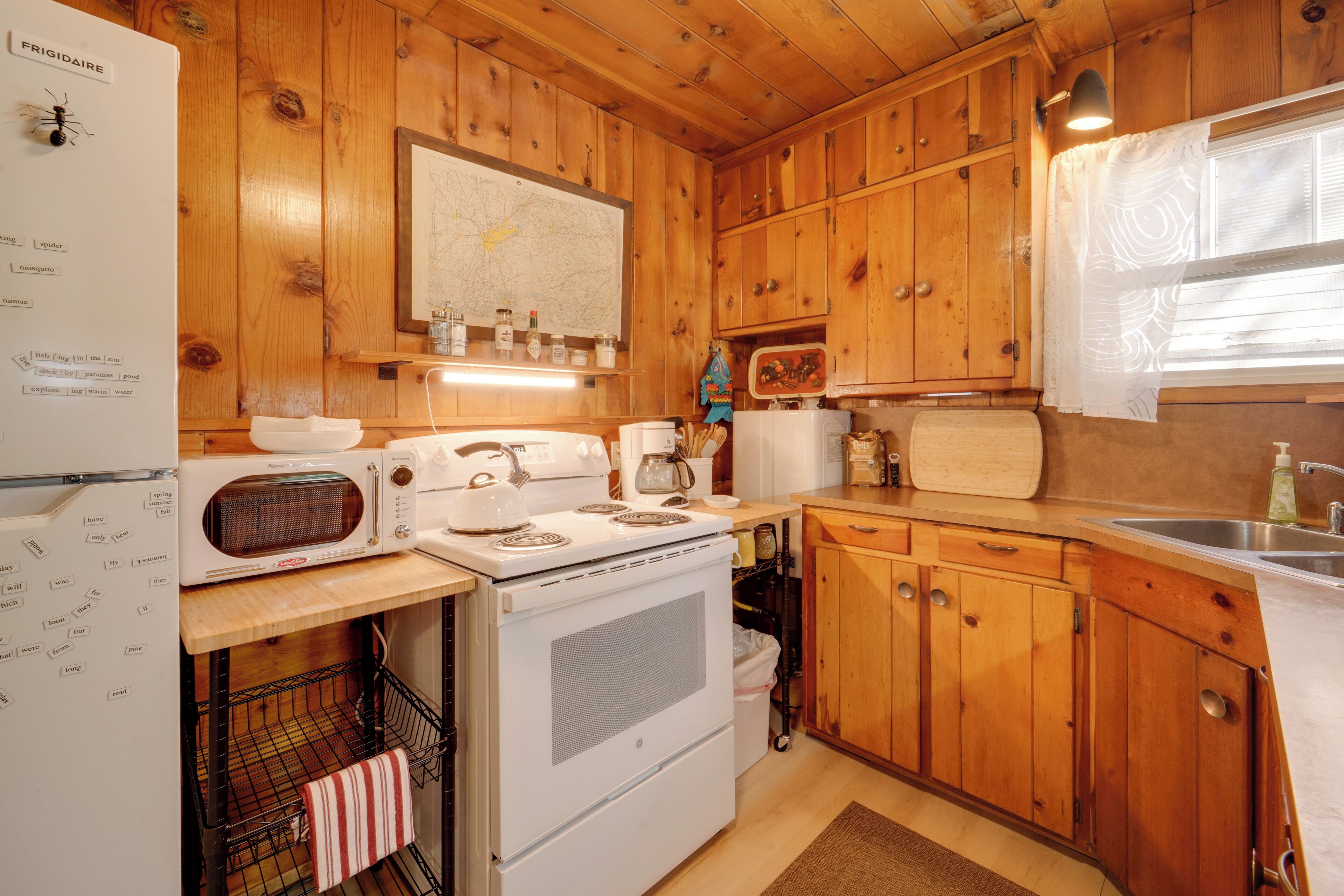 Une cuisine rustique, située dans une cabane en bois, équipée d’un réfrigérateur, d’une cuisinière, d’un four à micro-ondes et de meubles de rangement en bois.