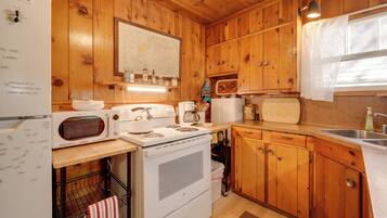 Une cuisine rustique, située dans une cabane en bois, équipée d’un réfrigérateur, d’une cuisinière, d’un four à micro-ondes et de meubles de rangement en bois.