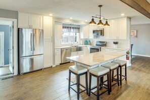 A modern kitchen with stainless steel appliances, a large island with bar stools, and a window with curtains. - Cozy Home Near Table Rock & Eureka Springs (Eureka Springs)
