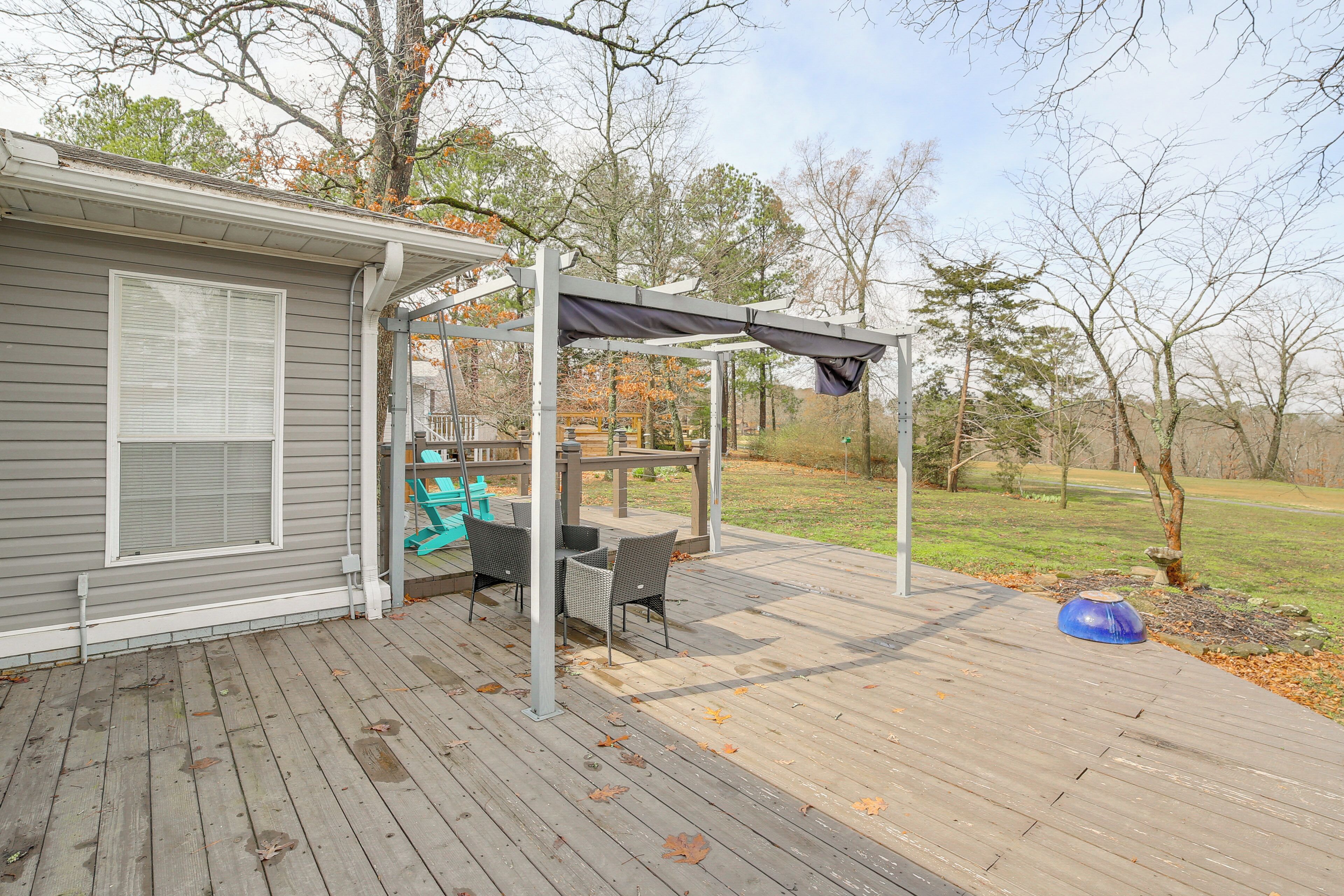A covered outdoor deck with a table and chairs, a pergola, and a view of the surrounding trees.