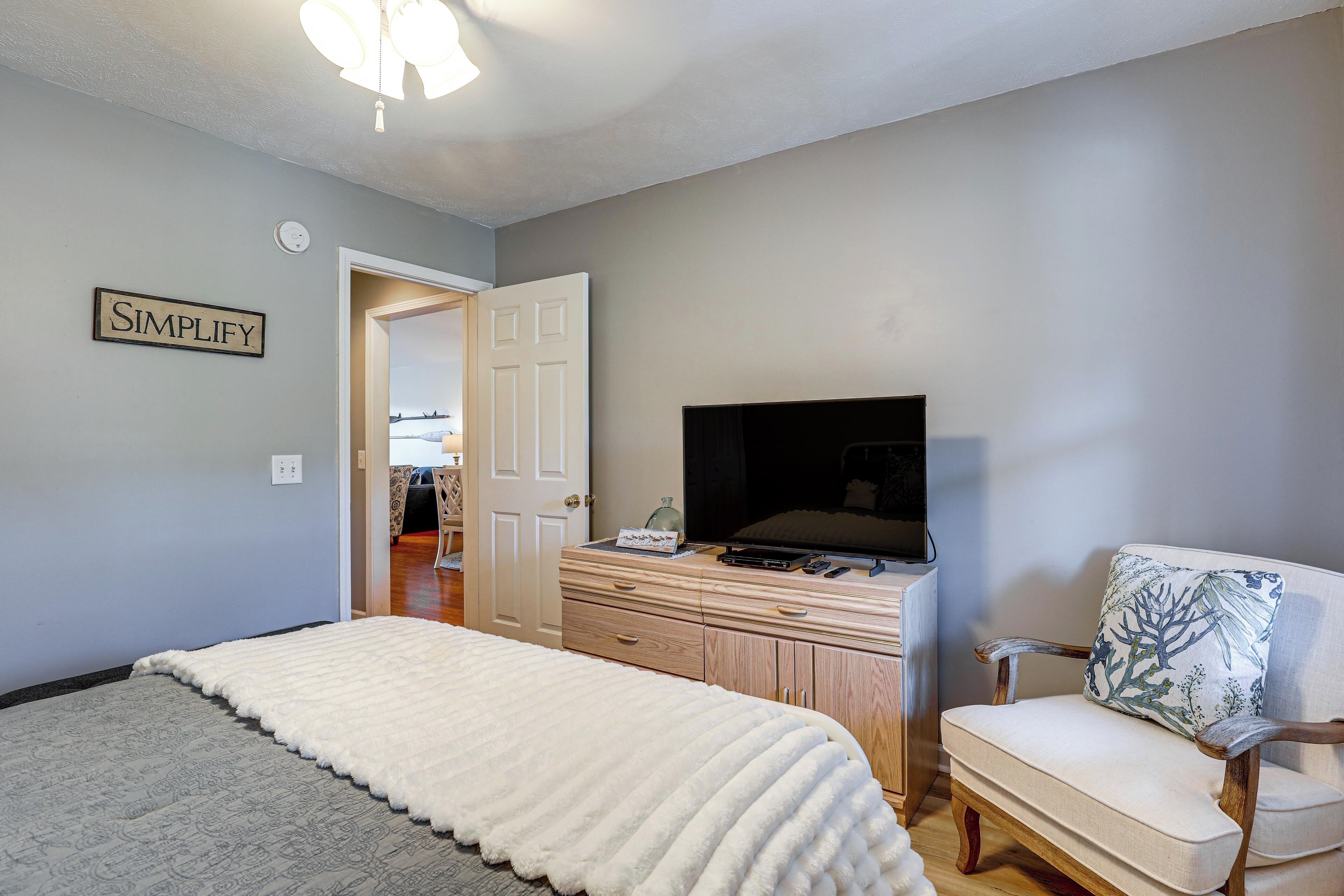A bedroom with a bed, a dresser, a television, and a chair.