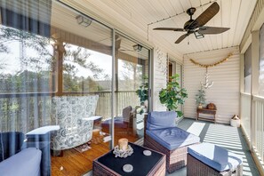 Une véranda aménagée avec des meubles en osier, un ventilateur de plafond et une vue sur l’extérieur.