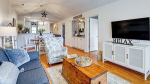 Ein Wohnzimmer mit Sofa, Sesseln, Couchtisch und Fernseher auf einem Schrank.