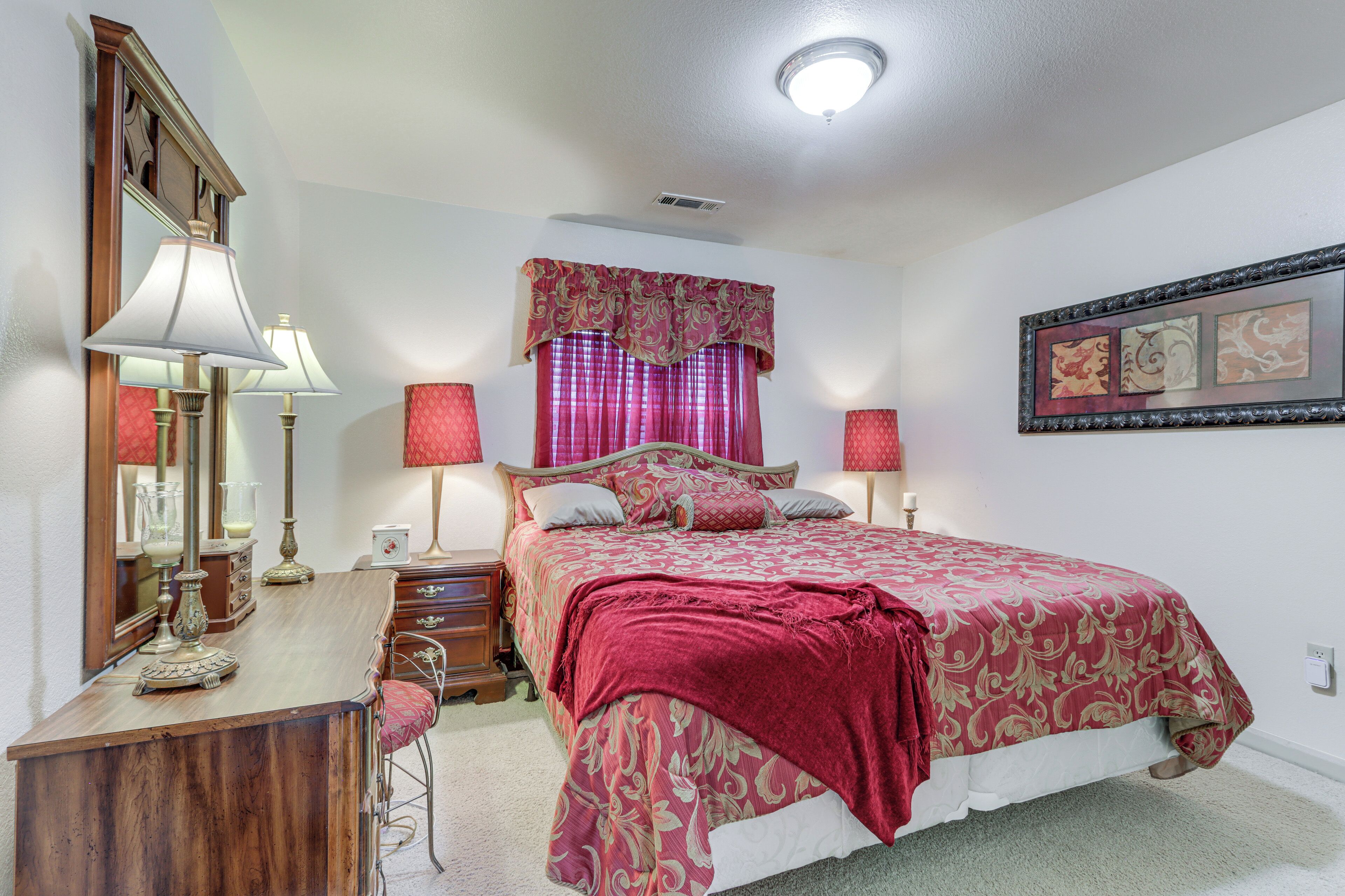 Une chambre à coucher avec un lit, des lampes de chevet, une commode, un miroir et une fenêtre avec des rideaux.