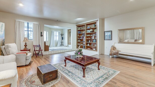 A spacious living room with a sofa, a coffee table, a bookshelf, and a large window.