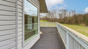 A covered outdoor area with a wooden deck, a window, and a view of a grassy field and trees.