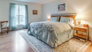 A bedroom with a bed, a nightstand, a chair, a window with curtains, and a ceiling fan.
