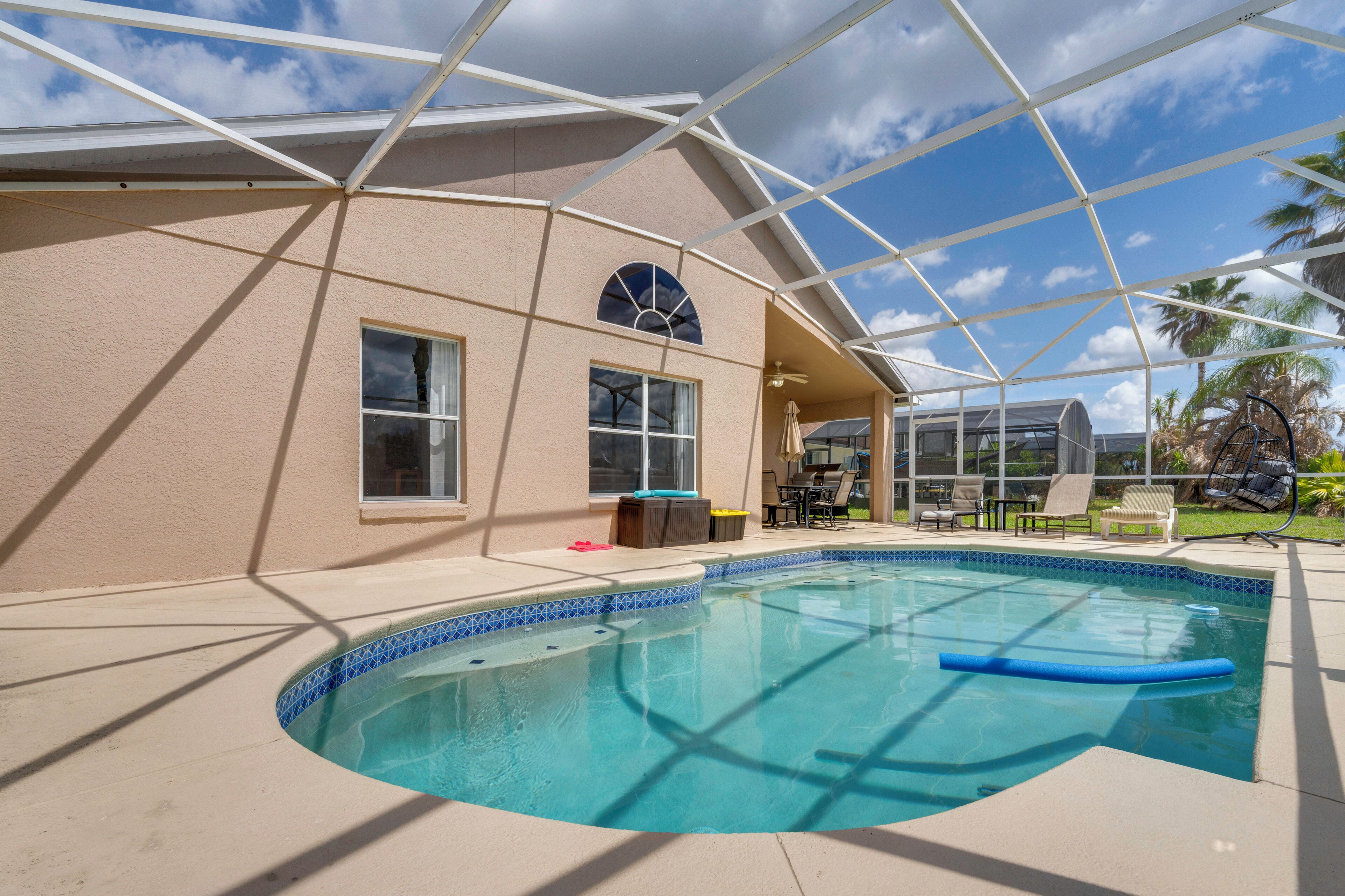 A swimming pool with a glass enclosure, a patio area with outdoor furniture, and a view of the sky.